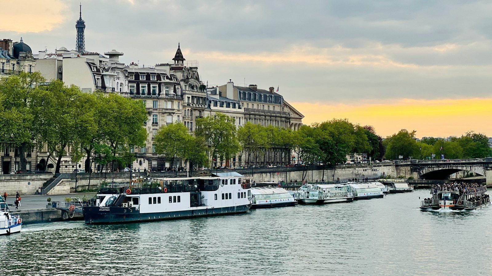 Bateaux et péniches à quai sur la Seine à Paris au coucher du soleil, façades haussmanniennes et Tour Eiffel en arrière-plan